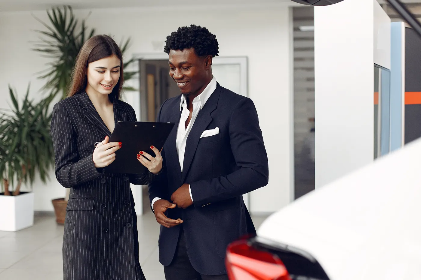 Two professionals reviewing a document beside a car